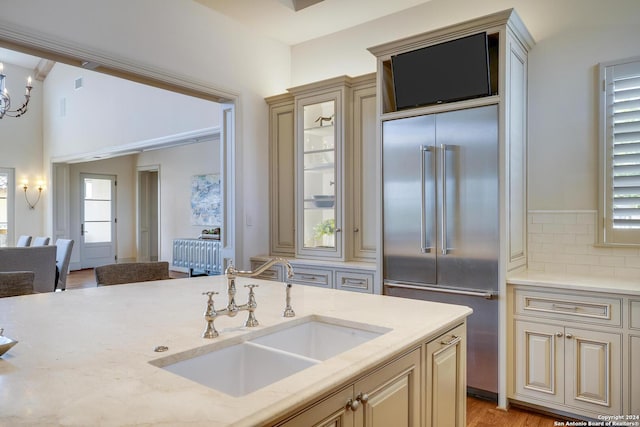 kitchen with light stone counters, sink, cream cabinets, and built in fridge