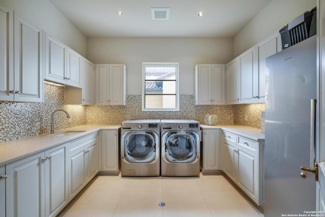 clothes washing area with sink, light tile patterned floors, washer and clothes dryer, and cabinets