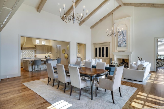 dining space with light hardwood / wood-style flooring, high vaulted ceiling, a premium fireplace, and a chandelier