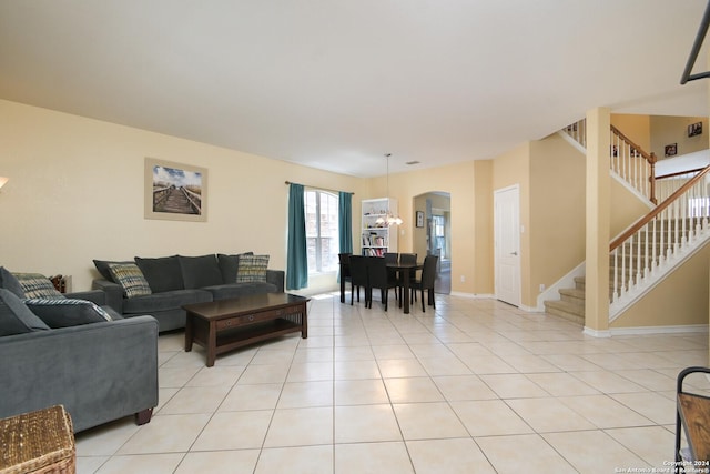 living area featuring arched walkways, light tile patterned flooring, a notable chandelier, baseboards, and stairs