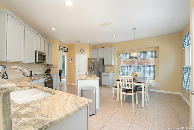 kitchen featuring backsplash, light tile patterned floors, appliances with stainless steel finishes, decorative light fixtures, and light stone counters