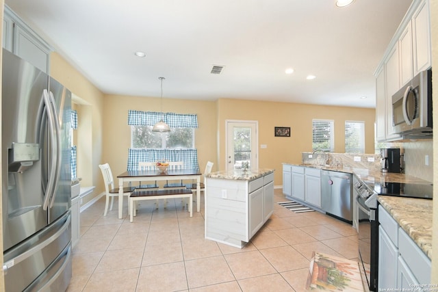 kitchen featuring stainless steel appliances, a kitchen island, tasteful backsplash, decorative light fixtures, and light tile patterned floors