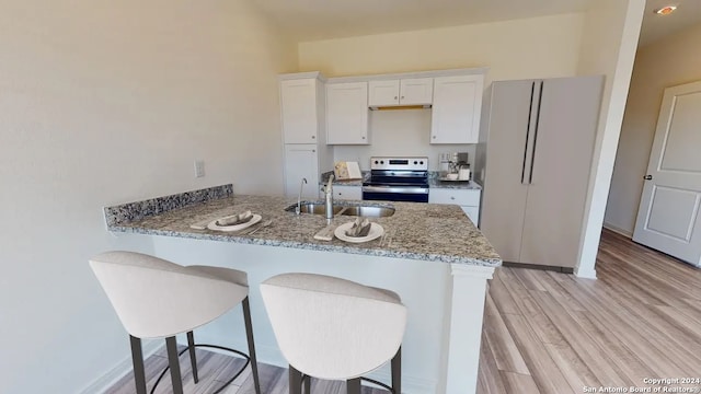 kitchen with light hardwood / wood-style flooring, electric range, light stone counters, sink, and white cabinetry