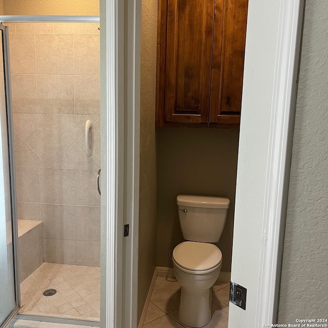 bathroom featuring tile patterned floors, a shower with shower door, and toilet