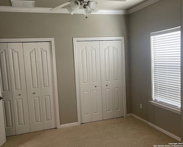 unfurnished bedroom featuring light carpet, ornamental molding, ceiling fan, and multiple closets