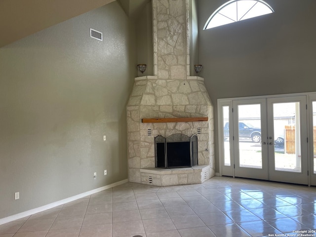 unfurnished living room featuring a towering ceiling, french doors, light tile patterned floors, and a stone fireplace