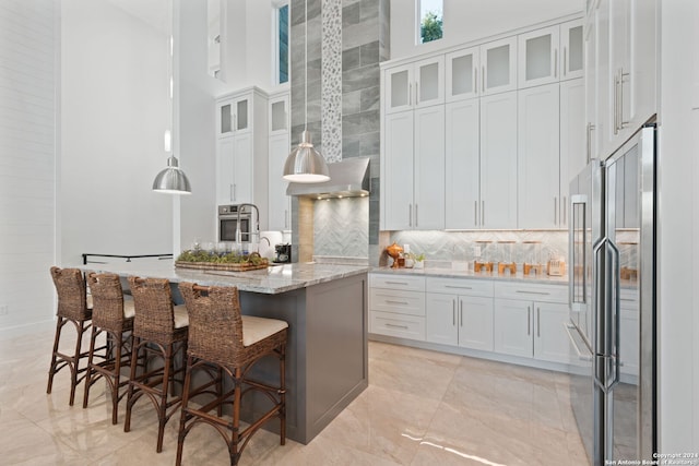 kitchen featuring a towering ceiling, a breakfast bar area, a center island with sink, white cabinets, and appliances with stainless steel finishes