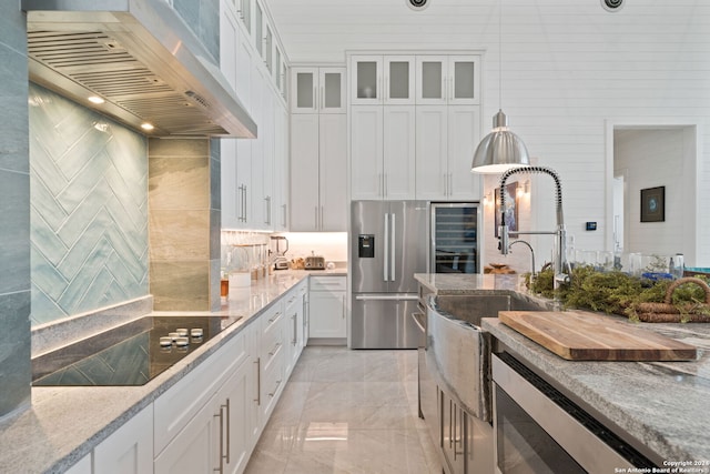 kitchen with white cabinetry, wall chimney range hood, stainless steel fridge with ice dispenser, light stone counters, and black electric stovetop