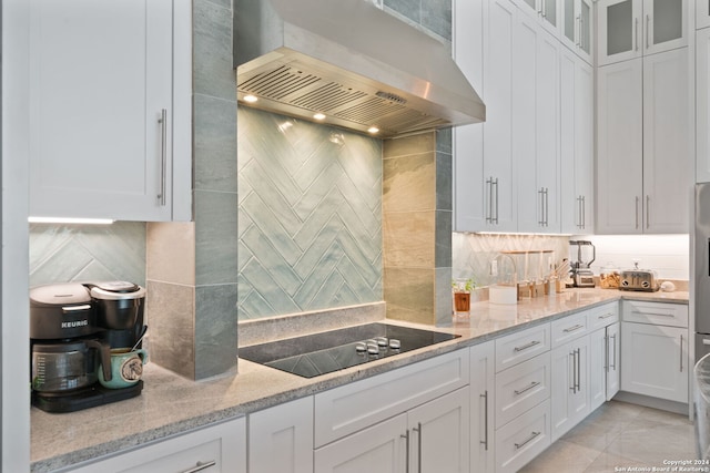 kitchen with light stone countertops, black electric stovetop, white cabinetry, and wall chimney exhaust hood