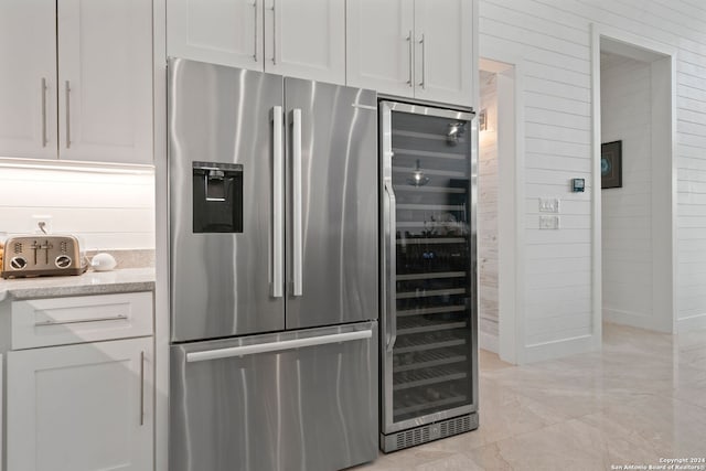 kitchen featuring stainless steel fridge with ice dispenser, white cabinetry, beverage cooler, and wood walls