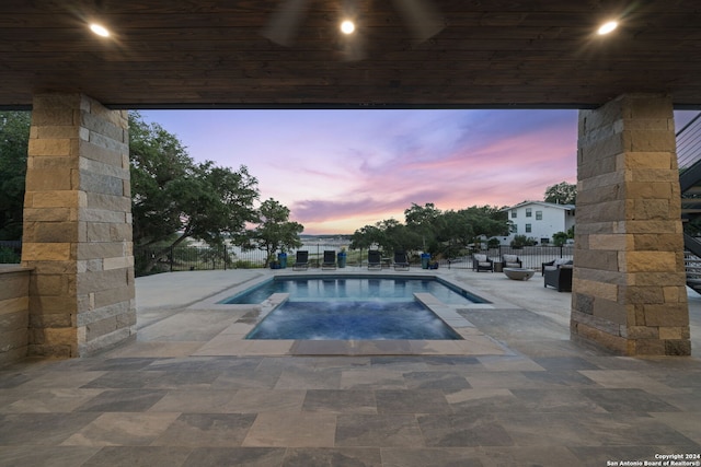 pool at dusk featuring an in ground hot tub and a patio