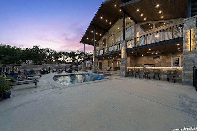 pool at dusk featuring a bar, a patio, and ceiling fan