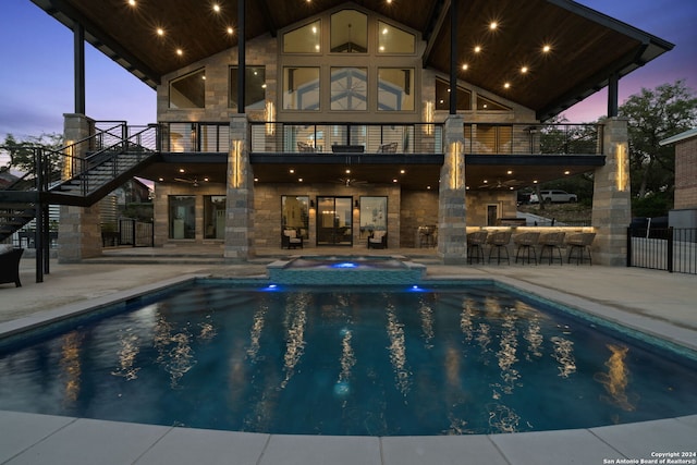 pool at dusk with an in ground hot tub, a patio, and an outdoor bar