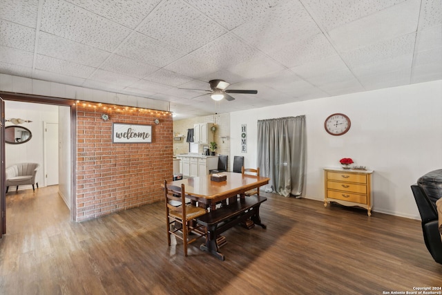 dining room with dark hardwood / wood-style flooring, ceiling fan, and brick wall