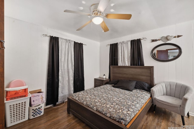 bedroom featuring dark wood-type flooring, ceiling fan, and wooden walls