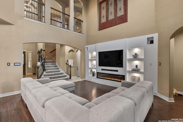 living room featuring dark hardwood / wood-style floors, a towering ceiling, and built in shelves