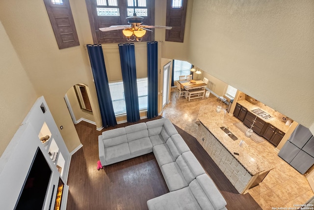 living room featuring a towering ceiling, ceiling fan, and dark wood-type flooring