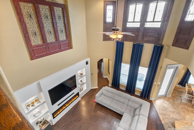 living room featuring hardwood / wood-style floors, ceiling fan, built in shelves, and a high ceiling