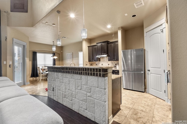 kitchen with decorative backsplash, a kitchen bar, dark brown cabinetry, pendant lighting, and stainless steel refrigerator