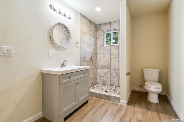 bathroom with hardwood / wood-style flooring, toilet, a tile shower, and vanity