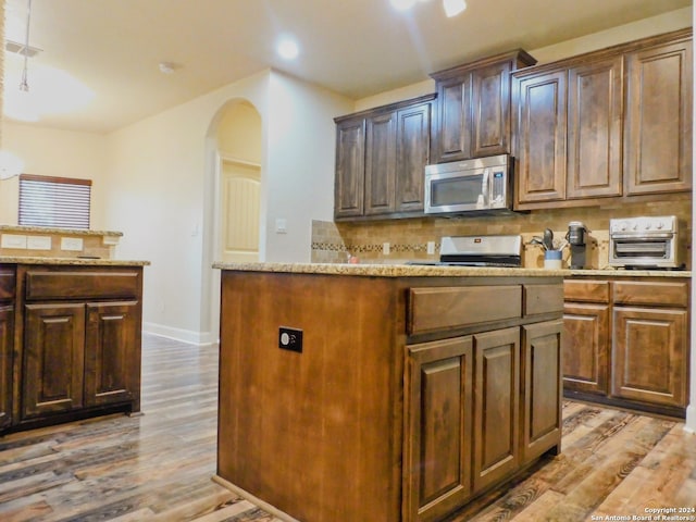 kitchen with backsplash, hardwood / wood-style floors, stove, and light stone counters