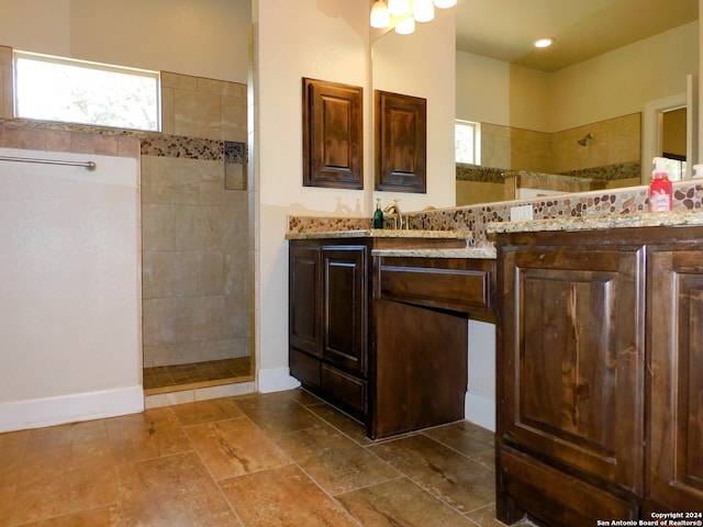 bathroom with tile floors, a healthy amount of sunlight, tiled shower, and vanity with extensive cabinet space