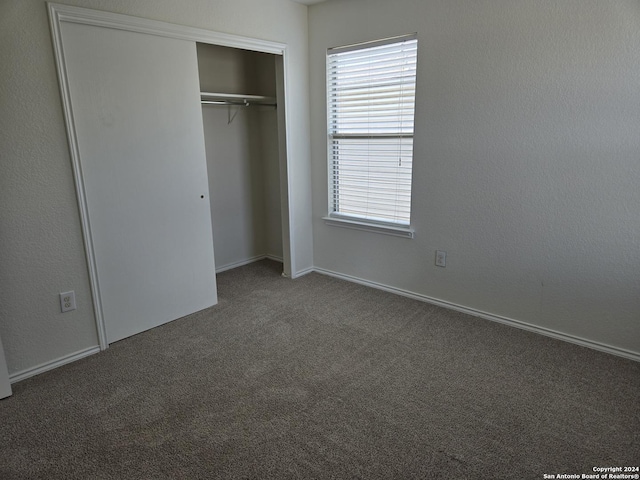 unfurnished bedroom with dark carpet and a closet