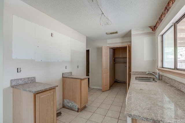 kitchen with a textured ceiling, light brown cabinets, light tile patterned flooring, and sink