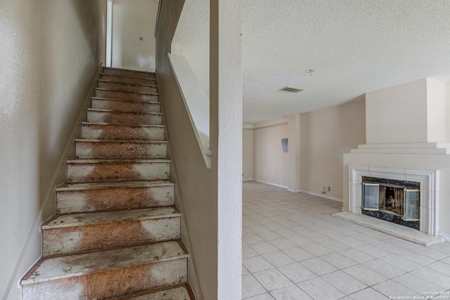 staircase featuring tile patterned floors, a fireplace, and a textured ceiling