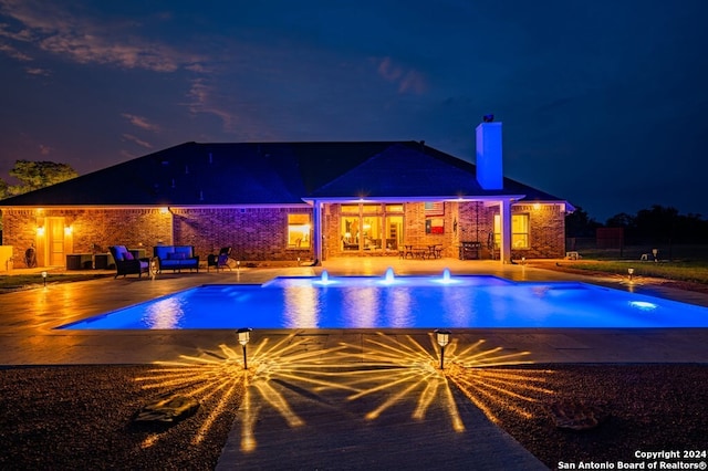 pool at night with pool water feature and a patio