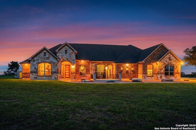 back of property at dusk with stone siding and a yard