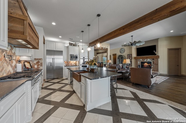 kitchen featuring a kitchen island with sink, built in appliances, ceiling fan, a breakfast bar area, and white cabinets