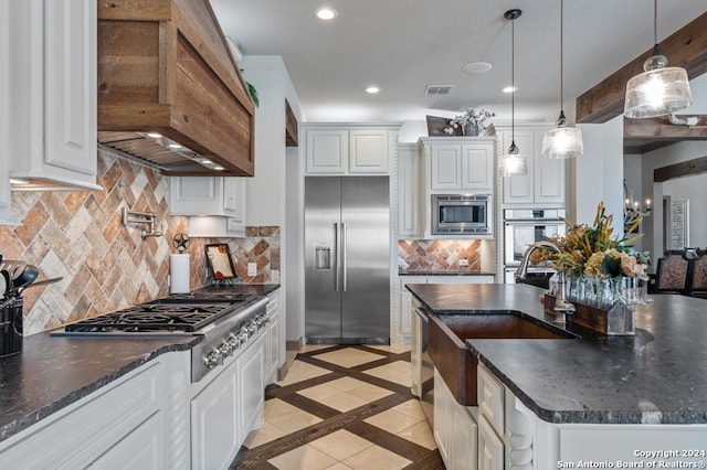 kitchen with white cabinets, dark stone countertops, hanging light fixtures, premium range hood, and built in appliances