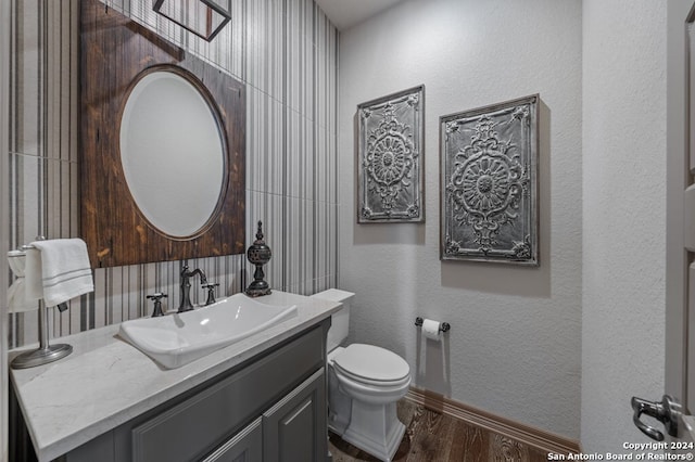 bathroom with vanity, toilet, a textured wall, baseboards, and wood finished floors