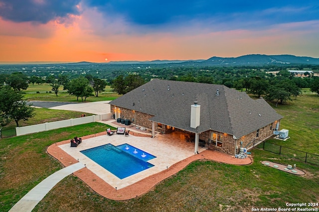 pool at dusk with a fenced backyard, a mountain view, a yard, and a patio