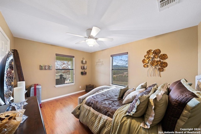bedroom with hardwood / wood-style floors, visible vents, baseboards, and a ceiling fan