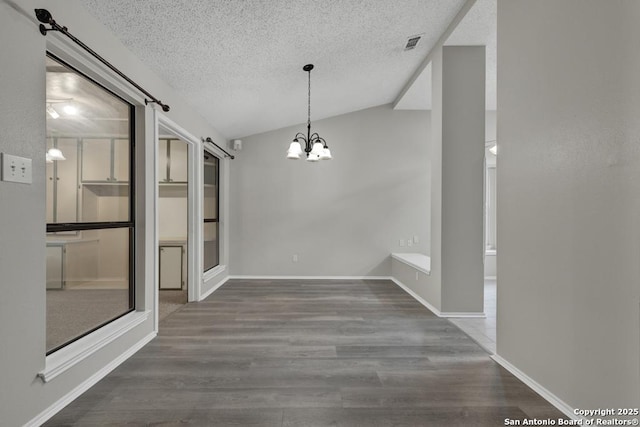 unfurnished dining area featuring an inviting chandelier, a barn door, dark hardwood / wood-style flooring, a textured ceiling, and lofted ceiling