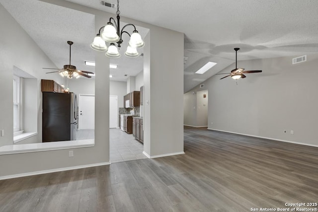 unfurnished living room with a textured ceiling, ceiling fan with notable chandelier, lofted ceiling, and light wood-type flooring