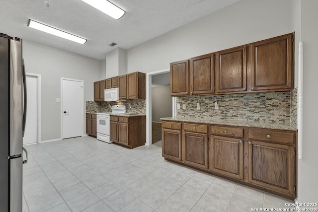 kitchen featuring light stone counters, white appliances, backsplash, and light tile patterned floors