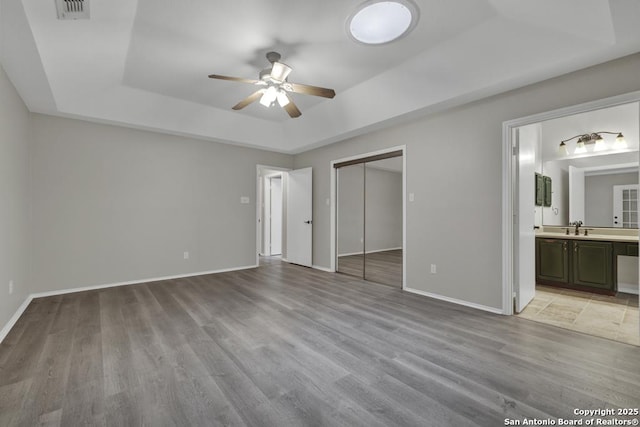 unfurnished bedroom featuring light wood-type flooring, a raised ceiling, ceiling fan, sink, and connected bathroom