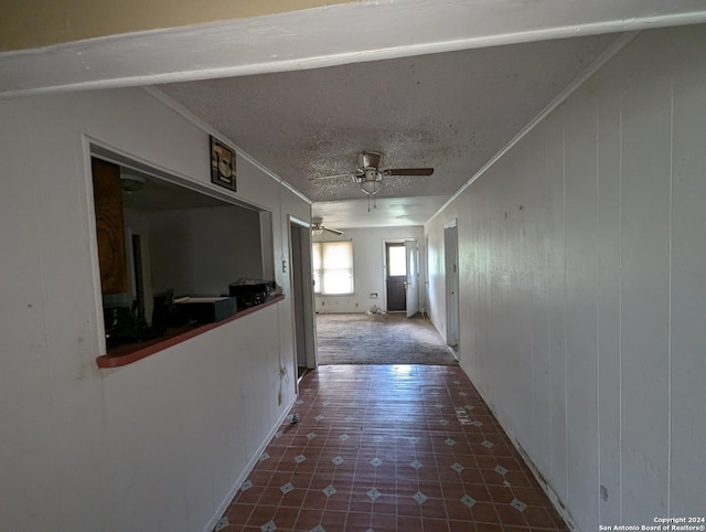 hallway featuring ornamental molding, a textured ceiling, and wooden walls