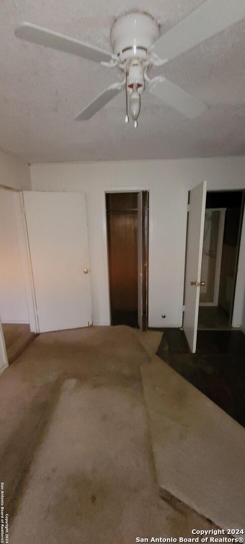 unfurnished bedroom featuring ceiling fan, dark carpet, and two closets