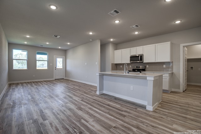 kitchen featuring light hardwood / wood-style flooring, a kitchen island with sink, backsplash, white cabinets, and appliances with stainless steel finishes