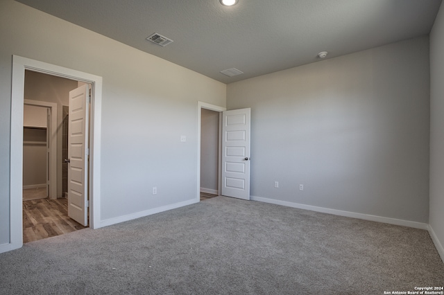 unfurnished bedroom with a walk in closet, a closet, and light colored carpet