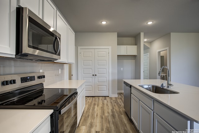 kitchen featuring appliances with stainless steel finishes, light wood-type flooring, sink, white cabinetry, and tasteful backsplash