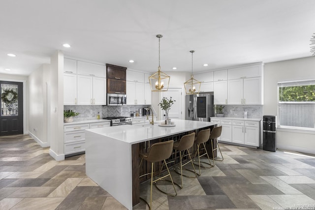 kitchen featuring a center island with sink, a kitchen breakfast bar, appliances with stainless steel finishes, tasteful backsplash, and white cabinetry