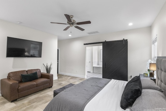 bedroom with a barn door, ensuite bathroom, ceiling fan, and light hardwood / wood-style floors