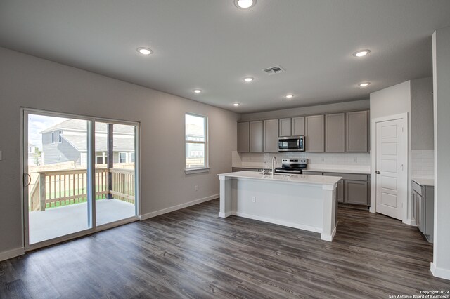 kitchen with stainless steel appliances, tasteful backsplash, dark hardwood / wood-style floors, gray cabinets, and a kitchen island with sink