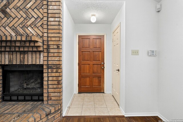 foyer entrance with a textured ceiling, a brick fireplace, and light tile floors