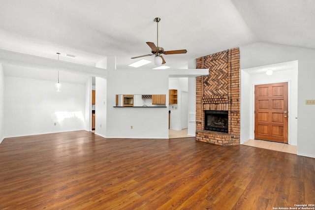 unfurnished living room with brick wall, lofted ceiling, a brick fireplace, wood-type flooring, and ceiling fan